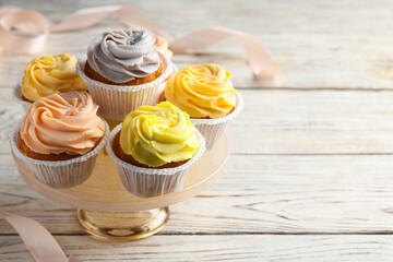 Stand with tasty cupcakes on white wooden table. Space for text