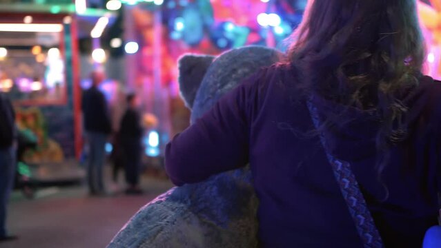 woman holding big plushie animal's at fun fair, loads of flashing lights around.