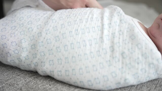 Close up of newborn baby being swaddled in a blanket in home by mother