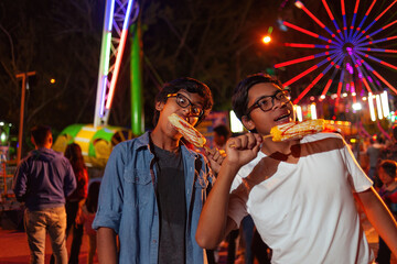 Happy Latino children eating corn on the cob at the fair with a Ferris wheel behind them.