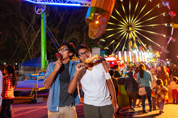Happy Latino boys eating at the fair with a Ferris wheel behind them.
