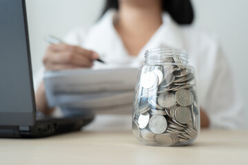 Savings concept coins in jar and woman check expenses list with laptop. Bills payment from savings...