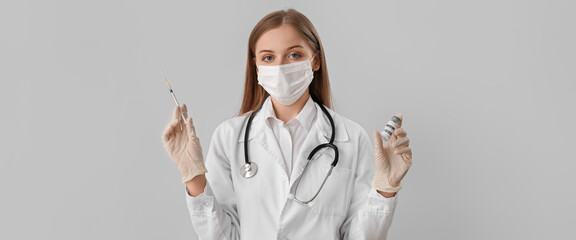 Female doctor with monkeypox vaccine and syringe on light background