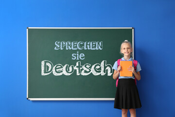 Little schoolgirl near blackboard with text SPRECHEN SIE DEUTSCH? (DO YOU SPEAK GERMAN?) in...