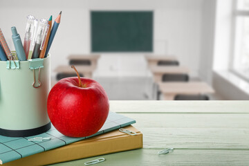 Set of school supplies and red apple on table in classroom