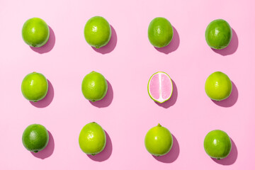 One cut lime among whole ones on pink background. Concept of uniqueness