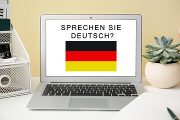 Modern laptop with text SPRECHEN SIE DEUTSCH? (DO YOU SPEAK GERMAN?) on screen at workplace