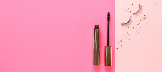 Black mascara and fake eyelashes on pink background with space for text