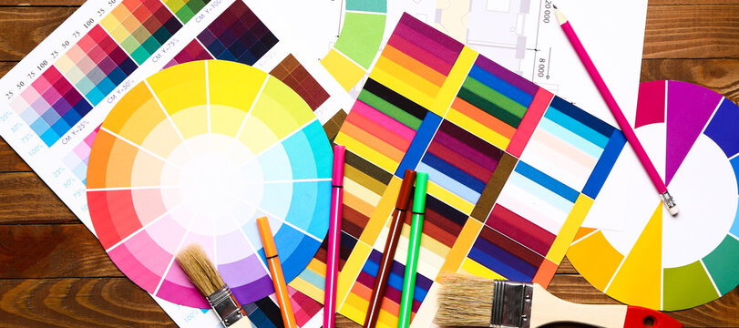 Color palettes with building plan and paint brushes on wooden background, top view