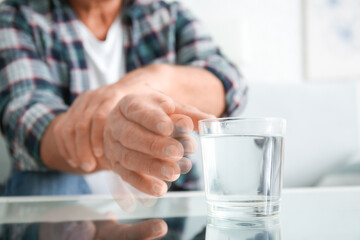 Senior man with Parkinson syndrome taking glass of water from table, closeup - obrazy, fototapety, plakaty