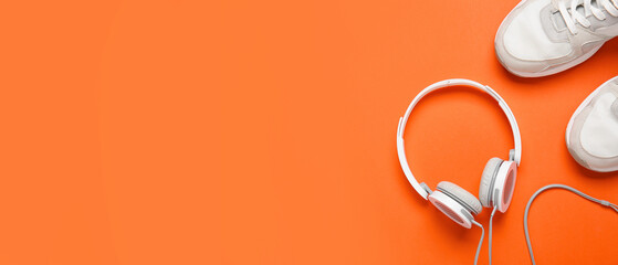 Sports shoes with headphones on orange background with space for text