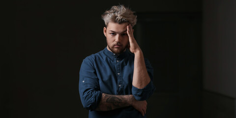 Depressed young tattooed man on dark background