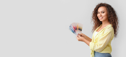 Beautiful young African-American woman holding color palettes on light background with space for text