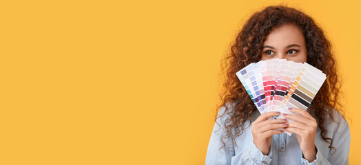 Beautiful young African-American woman holding color palettes on yellow background with space for...