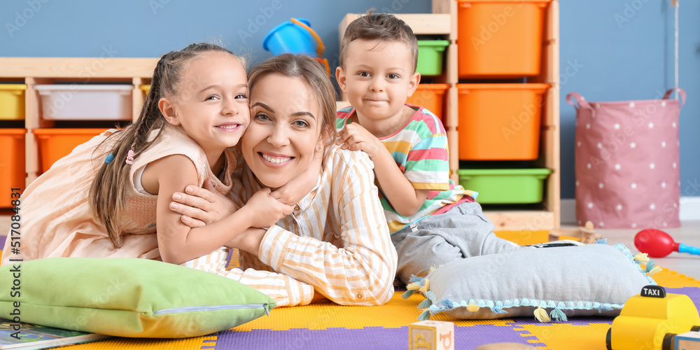 Sticker nanny and cute little children in playroom