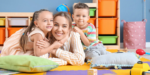 Nanny and cute little children in playroom - obrazy, fototapety, plakaty