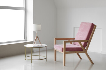 Comfortable armchair with table and lamp near light wall in room