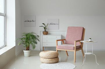 Comfortable armchair with table and houseplants near light wall in room