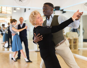 Elderly woman learning ballroom dancing in pair in dance studio