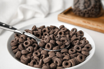 Bowl with black cereal rings and spoon on light background, closeup