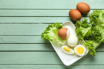 Plate with boiled chicken eggs and lettuce on color wooden background