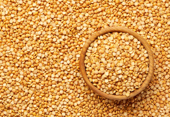 wooden plate with dried peas on a yellow peas background close-up top view.