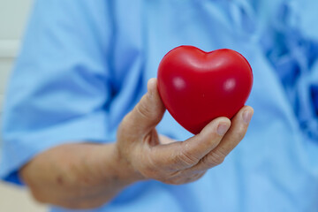 Asian elder senior woman patient holding red heart in hospital.