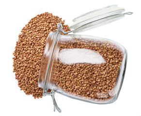 Raw dry buckwheat spill out of a glass storage jar isolated on white background top view.