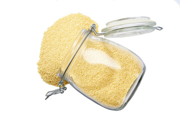 Raw dry couscous spill out of a glass storage jar isolated on white background top view.