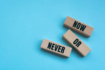 Now or never words on wooden blocks on blue background.