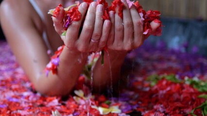 A woman relaxes in a spa hotel in a bathtub with red and pink flowers. Aroma therapy concept with...