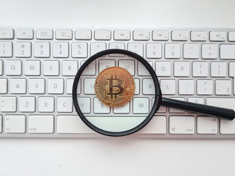 Bitcoin pending, magnifying glass and bitcoin coin on white computer keyboard