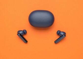 Wireless blue headphones and a closed charging box on an orange background. A popular wireless gadget.