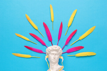 A statuette in yellow headphones on a blue background with red and yellow feathers. Minimalism.