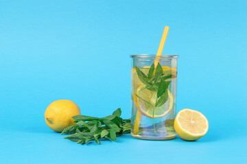 Water with lemon and mint in a glass with a cocktail tube on a blue background.