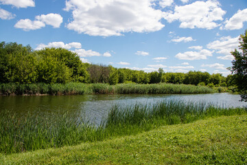 Landscape. River, along green banks, blue sky with clouds.