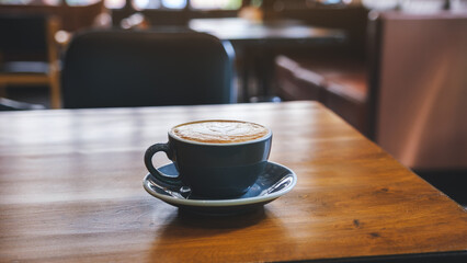 Closeup image of a cup of hot latte coffee with latte art on wooden table in cafe