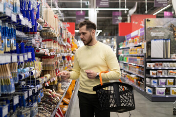 a man in a construction hypermarket with a grocery cart picks up brushes and rollers for painting...