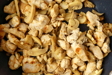 Chopped chicken fillet with mushroom fried on frying pan. Cooking process close up.
