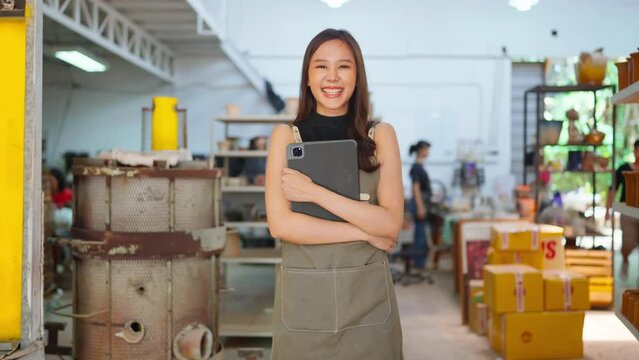 Asia female ceramist with apron hand arrange her clay sculp product on the shelf waiting for bake in oven,asian woman small business ceramic workshop owner smiling proud to present her new collection 