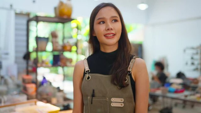 Asia female ceramist with apron hand arrange her clay sculp product on the shelf waiting for bake in oven,asian woman small business ceramic workshop owner smiling proud to present her new collection 