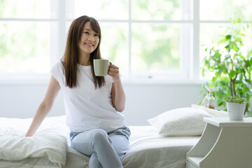 Obraz na płótnie Canvas ベッドに座ってコーヒーを飲む女性