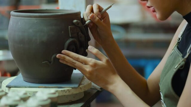 Close up of female hands working on potters wheel,asian female sculpture woman paitning coloring pattern detail design small vase bowl clay on potter's wheel  with concentrate and focus art therapy