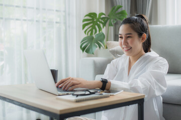 Smiling asian woman relax and sitting on sofa in living room using laptop for work, meeting. Happy young female use laptop talk on applications on gadget and Technology..