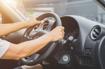 A young man sitting in a car with his hands on the steering wheel is driving to work.