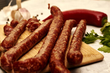 spicy smoked sausages on a cutting board next to red pepper garlic spices and herbs on the table