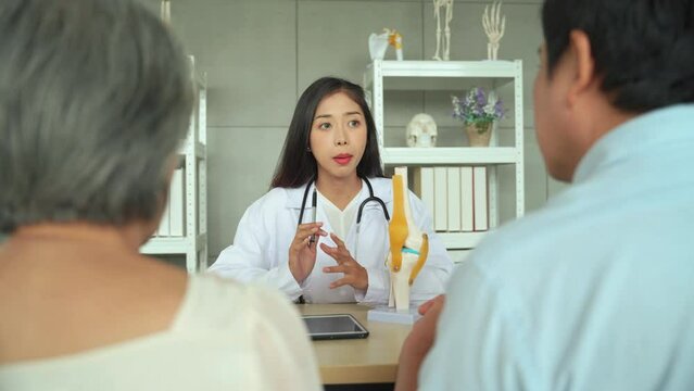 Specialist female doctor Explaining knee precautions and methods of treating the symptoms of elderly female patients. Female patient sitting and listening to advice with her son.