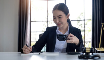 Professional Asian female lawyer working in her office, sipping a morning coffee while reading a law contract. cropped image