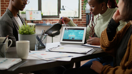 Diverse team of coworkers meeting to work on startup project, brainstorming ideas in boardroom and analyzing business charts on paperwork. Colleagues doing teamwork in company office.