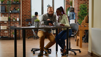 Diverse team of people working on business report in company office, analyzing charts information on documents and tablet. Man and woman meeting to plan collaboration in boardroom.